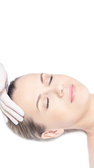 Naklejka premium Girl lying in cosmetology spa. Face massage. Doctor hand with protective glove near head. Medical skin care. White background. Close eyes. Rejuvenation procedure. Cream cosmetics. Vertical, copyspace