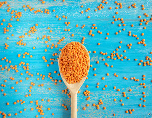 Red Lentils or Masoor Dal in wooden spoon on light blue background. Top view. Flat lay. Colorful...