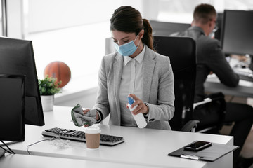 Businesswoman with medical mask disinfecting desk in the office..