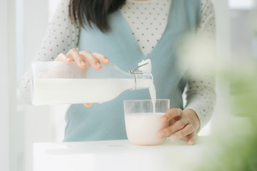 Fototapeta na wymiar Young beautiful pregnant asian woman pouring fresh milk from a bottle.