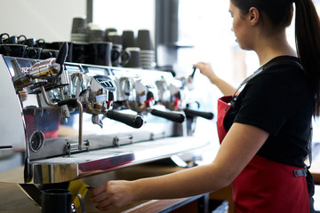 Fototapeta premium Cropped image of young woman working barista in coffee shop and preparing tasty espresso on modern coffee machine with metal professional equipment.Female waitress standing at automatic appliance