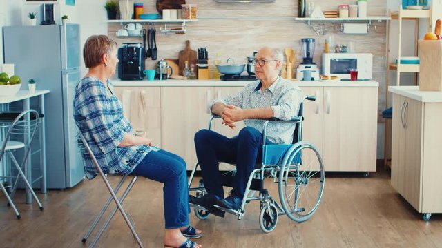 Happy senior woman talking with handicapped husband in wheelchair. Old woman having a conversation with husband. Living with disabled person with walking disabilities