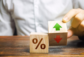 Businessman holds wooden blocks with percent and up or down arrow. Mortgage and loan rates....