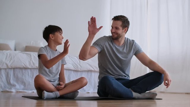 Family fitness at home, Father coach, Sports kid, Fun gymnastics. Cheerful man and boy go in for sports at home while sitting on the floor