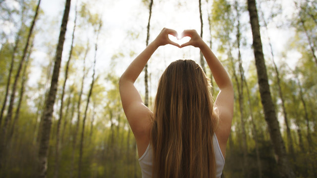 Woman framing sun with her hands in heart shape. Copy space. High quality photo
