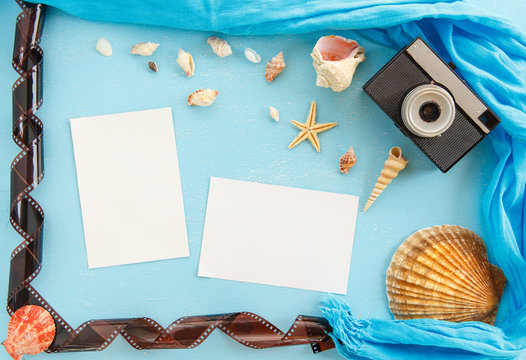 Blank paper photo frames with starfish, shells and items on wooden table.