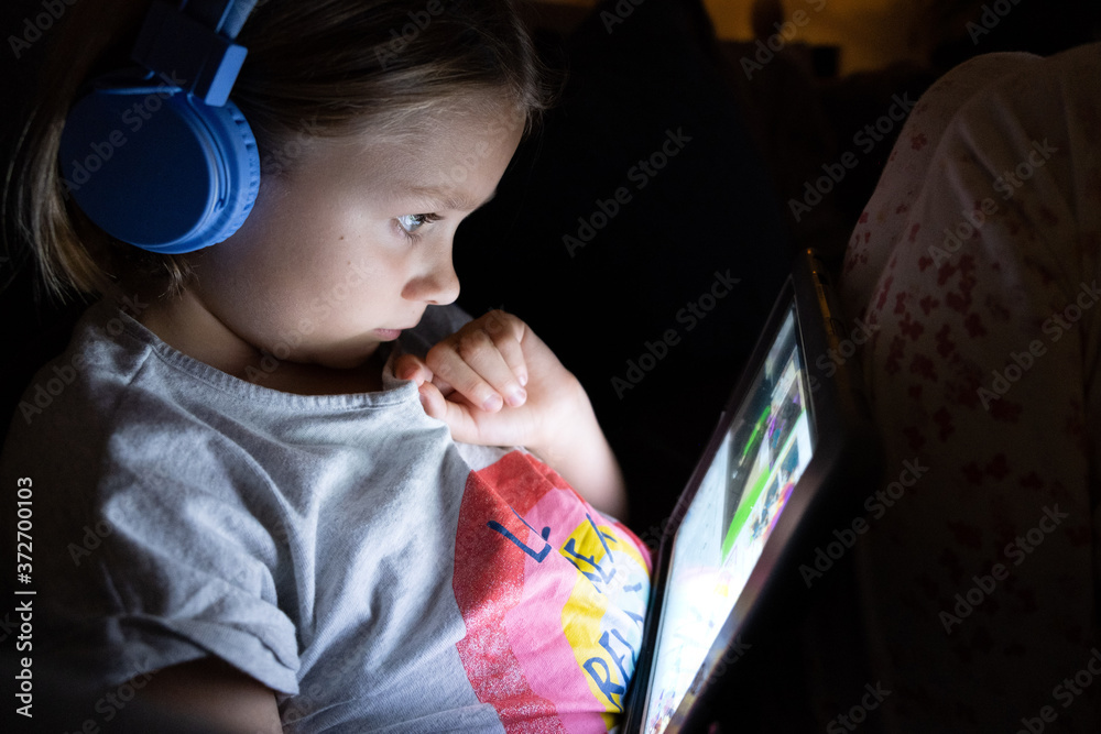 Wall mural little girl on a tablet with blue head phones in a dark room