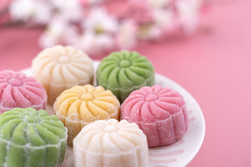 Colorful snow skin moon cake, sweet snowy mooncake, traditional savory dessert for Mid-Autumn Festival on pastel pale pink background, close up, lifestyle.
