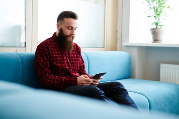 Smiling young  male sending messages to friends using application on digital tablet connected to 4G internet.Bearded hipster guy playing video games on gadget during recreation time in office