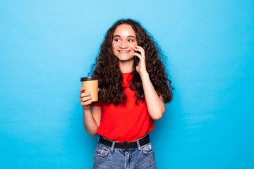 Fototapeta na wymiar Young woman holding coffee to take away and talk mobile over isolated blue background
