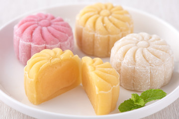 Colorful snow skin moon cake, sweet snowy mooncake, traditional savory dessert for Mid-Autumn Festival on bright wooden background, close up, lifestyle.