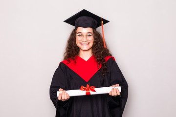 Beautiful college graduate wearing cap and gown holding diploma on white background