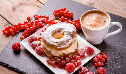 Cup of coffee, cake and red berries of raspberries and currants on a wooden table