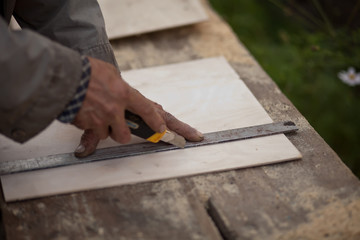 Senior elderly carpenter using a straightedge to draw a line on a board.