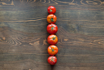 A set of six ripe tomatoes. Vegetables are located hardly one after another on a wooden table....