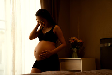 Close-up of a pregnant woman touching her belly on the foreground in emotional smile happy by asian...