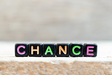 Black bead with color letter in word chance on wood background