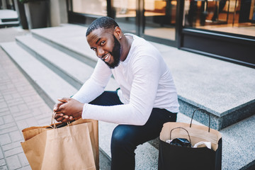 Portrait of afro american male hipster resting after shopping in mall sitting on stairs with paper...
