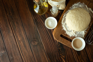Baking in rural kitchen. Dough and recipe ingredients on vintage brown wooden table. Top view. Rustic background