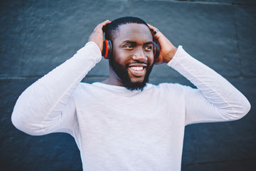 Cheerful afro american guy listening music in modern headphones satisfied with quality of sound,...