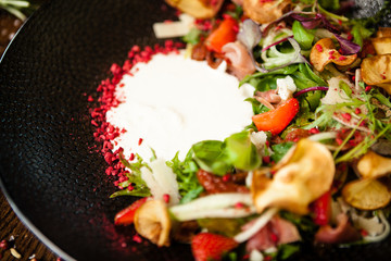 Crudo ham salad. Stracciatella and Grana Padano cheese, sundried tomato, fresh cucumber. Delicious healthy mixed greens food closeup served on a table for lunch in modern cuisine gourmet restaurant.