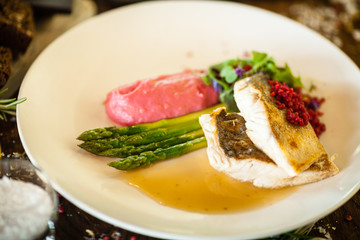 Pike-perch fillet. Asparagus, pearl couscous, white wine sauce, beet-flavored mashed potatoes. Delicious seafood fish closeup served on a table for lunch in modern cuisine gourmet restaurant