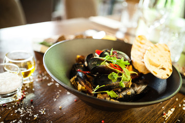 Blue mussels in white wine sauce in black bowl. Delicious healthy seafood closeup served on a table for lunch in modern cuisine gourmet restaurant