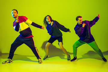 Wild moving. Stylish men and woman dancing hip-hop in bright clothes on green background at dance hall in neon light. Youth culture, movement, style and fashion, action. Fashionable portrait.