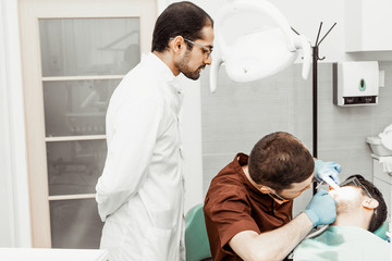 An intern dentist examines a patient under the supervision of a mentor. Professional uniform and...