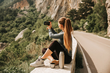 Traveling woman sitting near mountain and looking far away , making photo Spring weather, calm scene. Hiking outdoors, landscape view in the sunlight. A series of photos of Wanderlust.