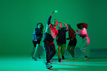 Selfie time. Stylish men and woman dancing hip-hop in bright clothes on green background at dance...
