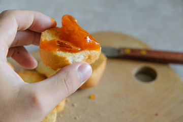 Toast with apricot jam in a man's hand on the background of the table.