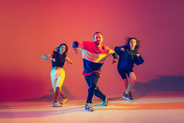 Dynamic. Stylish men and woman dancing hip-hop in bright clothes on green background at dance hall...