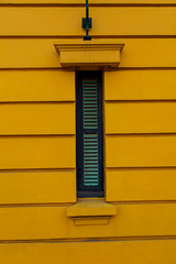 Persiana vertical y angosta de color verde en una pared amarilla