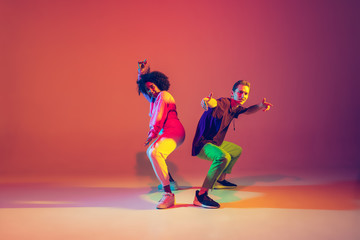 Summer. Stylish man and woman dancing hip-hop in bright clothes on green background at dance hall in neon light. Youth culture, movement, style and fashion, action. Fashionable portrait.