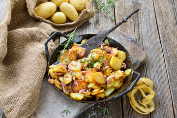 Deftige Bratkartoffeln mit Speck und Zwiebeln rustikal in der Eisenpfanne serviert – Hearty fried...
