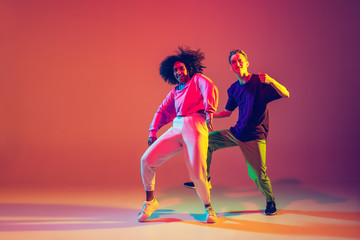 Drive in motion. Stylish man and woman dancing hip-hop in bright clothes on green background at...