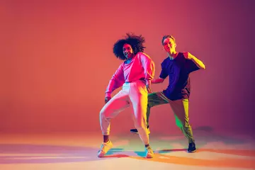 Foto op Aluminium Drive in motion. Stylish man and woman dancing hip-hop in bright clothes on green background at dance hall in neon light. Youth culture, movement, style and fashion, action. Fashionable portrait. © master1305