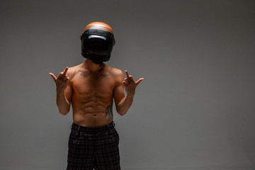 Athletic guy racer in helmet with naked torso stands in studio shows middle finger. Kart racing...