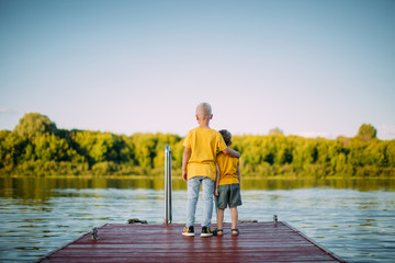 Cool kids brothers hug each other and look at the river staying on dock. Summertime photo about...