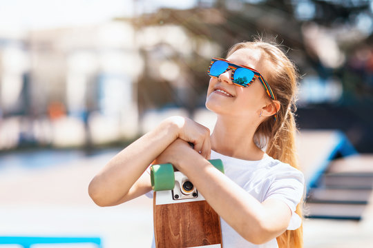 Satisfied teen girl with a skateboard in her hands and sunglasses looking up