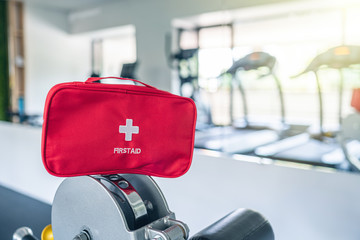 First aid kit red box in the fitness gym opposite the sport equipment and  jogging simulators. Healthy lifestyle, safety and help concept