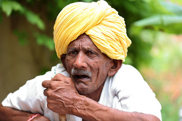 Amazed old Indian man wearing yellow turban looking up with mouth opened. Curious old man. Wearing traditional Indian clothes. Old man holding stick in hand. Old man waiting for his turn. 