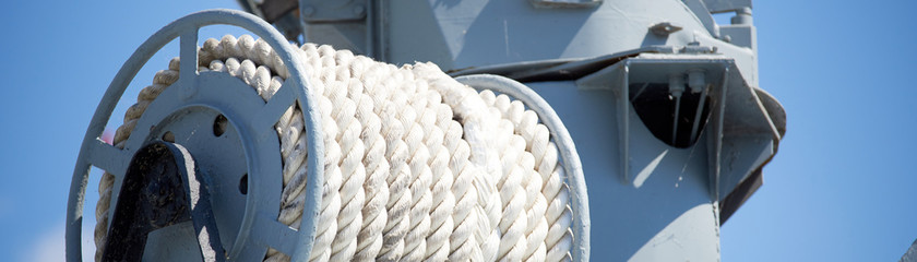 Cable reel with a white rope on the deck of the ship against blue sky. Logo template