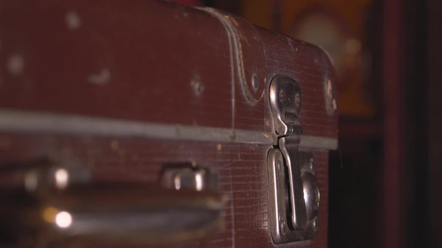 The man closes an old battered brown suitcase with metal latches.