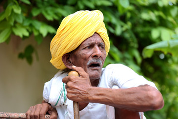 Amazed old Indian man wearing yellow turban looking up with mouth opened. Curious old man. Wearing traditional Indian clothes. Old man holding stick in hand. Old man waiting for his turn. 