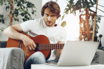 Young man watching guitar tutorial on his laptop