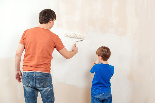 Happy family renovating their new home. Father showing his son how painting wall with a roller.