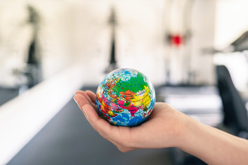 Toy globe in the female hand in fitness gym opposite the sport equipment and  jogging simulators. Healthy lifestyle. World health day. concept.