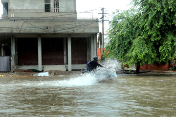 Jaipur,Rajasthan,India.14-August-2020. A female wearing mask and raincoat wading through water logged road on scooter. Normal life disrupted due to heavy rain. Heavy rains during covid-19 pandemic.